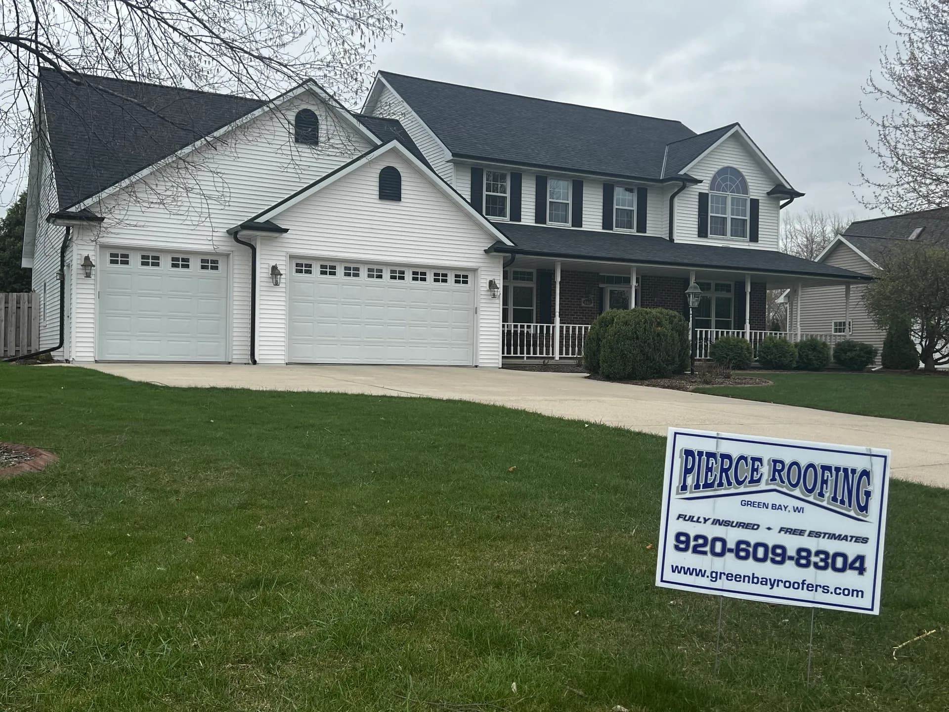 White two-story colonial with a new dark shingle roof and Pierce Roofing yard sign in Green Bay WI